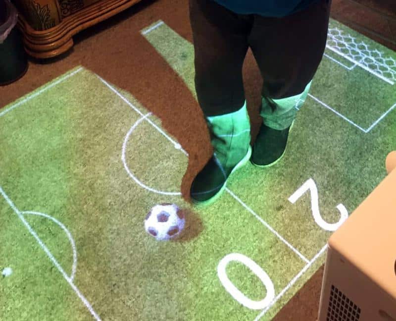young adult playing soccer with omi on floor