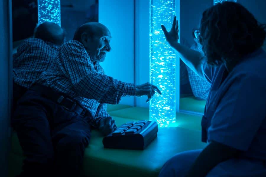 Elderly man with dementia with nurse in sensory room with bubble tube